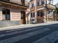 a cross walk on a busy residential street in europe, with buildings behind it and cars parked outside of the building