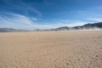 a very sparse desert plain on the side of a mountain, with a dust trail in front of the field