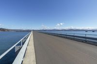 the concrete road is in an open area beside the water and a mountain range in the background