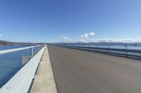 the concrete road is in an open area beside the water and a mountain range in the background