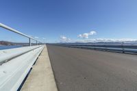 the concrete road is in an open area beside the water and a mountain range in the background