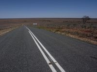 a lone road with no cars on it, surrounded by barren fields, in the outback