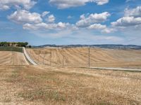 a field with dry grass and some power lines on it with clouds and a lone farm