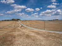 a field with dry grass and some power lines on it with clouds and a lone farm