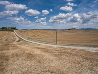 a field with dry grass and some power lines on it with clouds and a lone farm