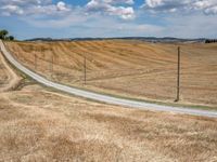 a field with dry grass and some power lines on it with clouds and a lone farm