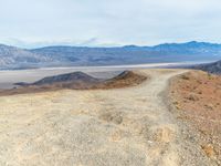 a dirt road winding through the desert near mountains of mountains in background and distant plain