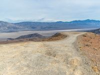 a dirt road winding through the desert near mountains of mountains in background and distant plain