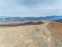 a dirt road winding through the desert near mountains of mountains in background and distant plain