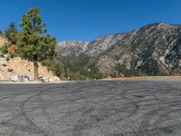 an empty road in front of the mountains with trees on either side and rocks piled on the top