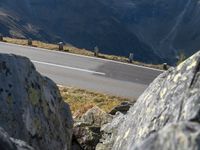 a man riding a motorcycle down a curvy road surrounded by mountains and rocks