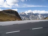 an empty highway in front of a mountains range with snow on top of the mountain