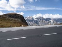 an empty highway in front of a mountains range with snow on top of the mountain