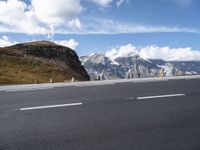 an empty highway in front of a mountains range with snow on top of the mountain