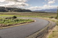 a paved country road winding off to the water and fields in the background with some trees