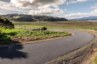 a paved country road winding off to the water and fields in the background with some trees