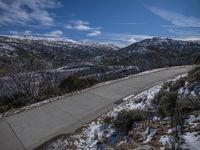 a paved country road is surrounded by snow covered mountains and shrubs in winter time with blue skies