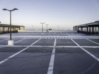 a empty parking lot with street lamps in the background - and a plane landing at the far end