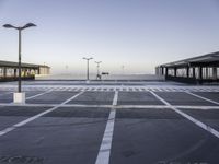 a empty parking lot with street lamps in the background - and a plane landing at the far end