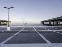 a empty parking lot with street lamps in the background - and a plane landing at the far end