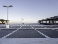 a empty parking lot with street lamps in the background - and a plane landing at the far end