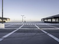 a empty parking lot with street lamps in the background - and a plane landing at the far end