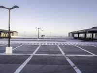 a empty parking lot with street lamps in the background - and a plane landing at the far end