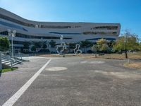 a parking lot next to a large building with glass windows and sculptures in front of it