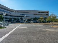 a parking lot next to a large building with glass windows and sculptures in front of it