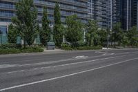 an empty road with buildings behind it in the distance in an urban area with green trees and bushes