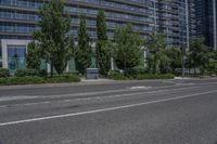 an empty road with buildings behind it in the distance in an urban area with green trees and bushes