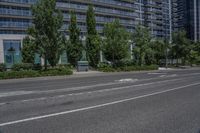 an empty road with buildings behind it in the distance in an urban area with green trees and bushes