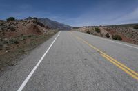 a lone motorcycle parked on the side of an empty road near mountains and hills in the background