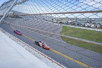 a car racing on a track by a fence with other cars at the finish line