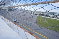 a car racing on a track by a fence with other cars at the finish line