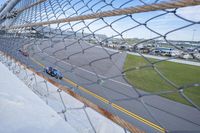 a car racing on a track by a fence with other cars at the finish line