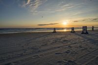 people standing on a beach at the ocean with sunset in the background and chairs arranged on the sand