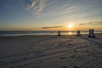 people standing on a beach at the ocean with sunset in the background and chairs arranged on the sand