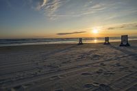 people standing on a beach at the ocean with sunset in the background and chairs arranged on the sand