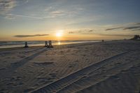 people standing on a beach at the ocean with sunset in the background and chairs arranged on the sand