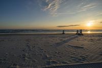 people standing on a beach at the ocean with sunset in the background and chairs arranged on the sand