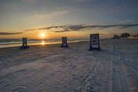 the sun is setting behind two signs on a beach near the ocean and beach chairs