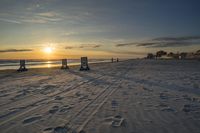 the sun is setting behind two signs on a beach near the ocean and beach chairs