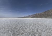 a flat plain in the desert with a bunch of mountains and snow on it under a blue sky