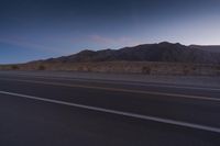 a view of the desert at sunset with mountains in the background to the right and two roads running down them