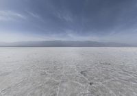 a desert with low clouds in the sky above it and a mountain range behind it