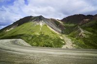the mountains are painted in bright green and brown colors, with gravel roads going down them