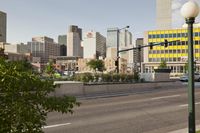 a long highway with two cars driving on it and tall buildings in the distance with trees in the foreground