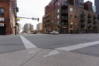 an intersection with street signs and car driving on the road near buildings on the other side