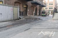 a green trash truck parked in a parking spot on a city street next to an industrial building